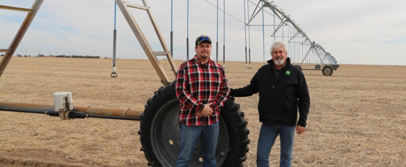 Kyle and Michael stan by a drive unit, which moves the sprinkler system in circle around a field.